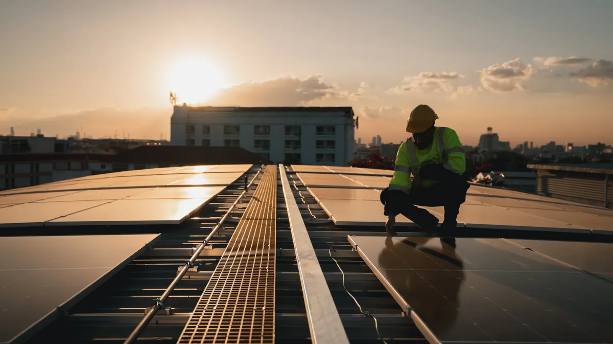 Technician inspects solar panels on an industrial roof at sunset.