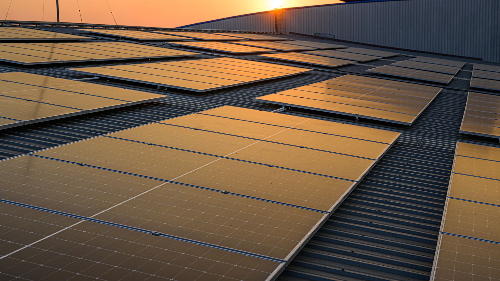 Solar panels on an industrial building roof at sunset.