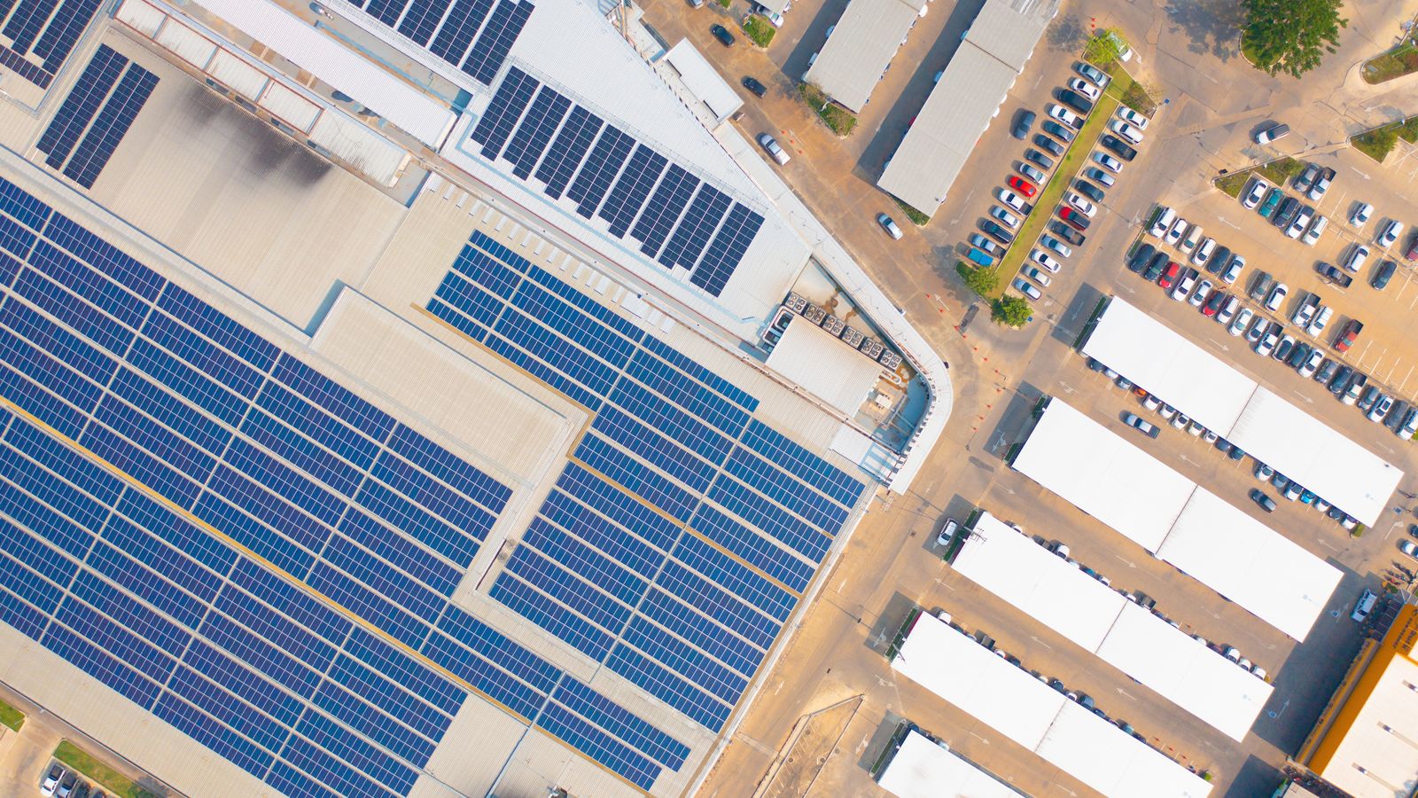Aerial view of industrial buildings with solar rooftops and a parking lot.