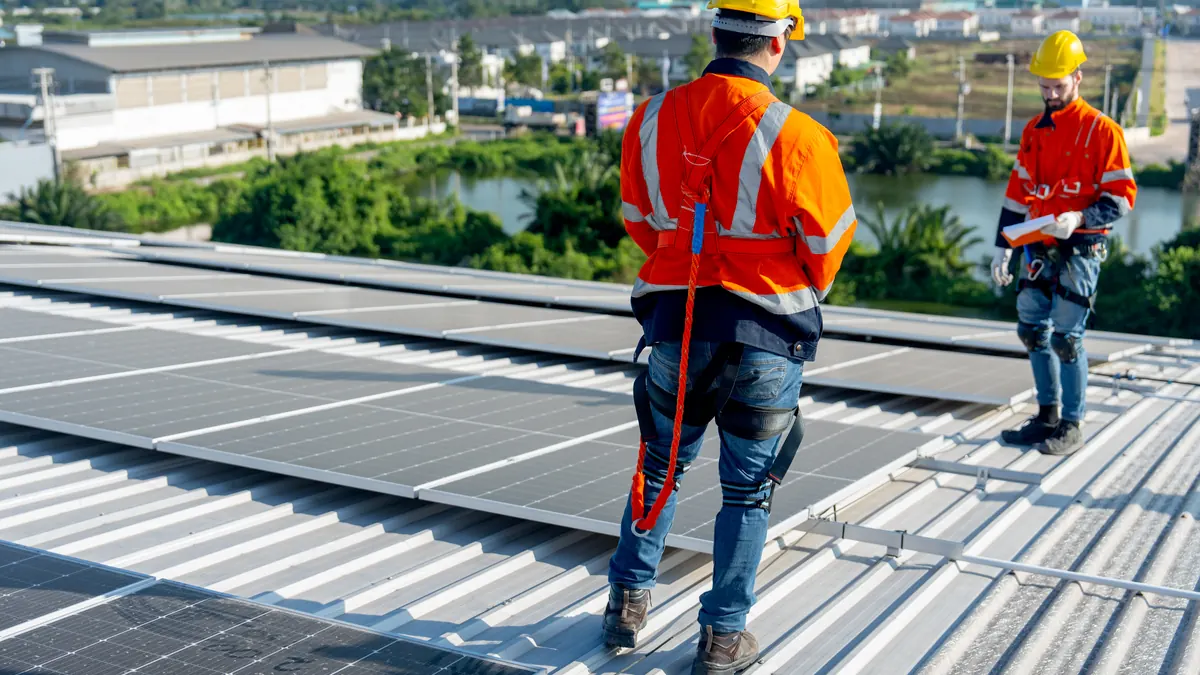 Installers in harnesses walk across a solar roof.