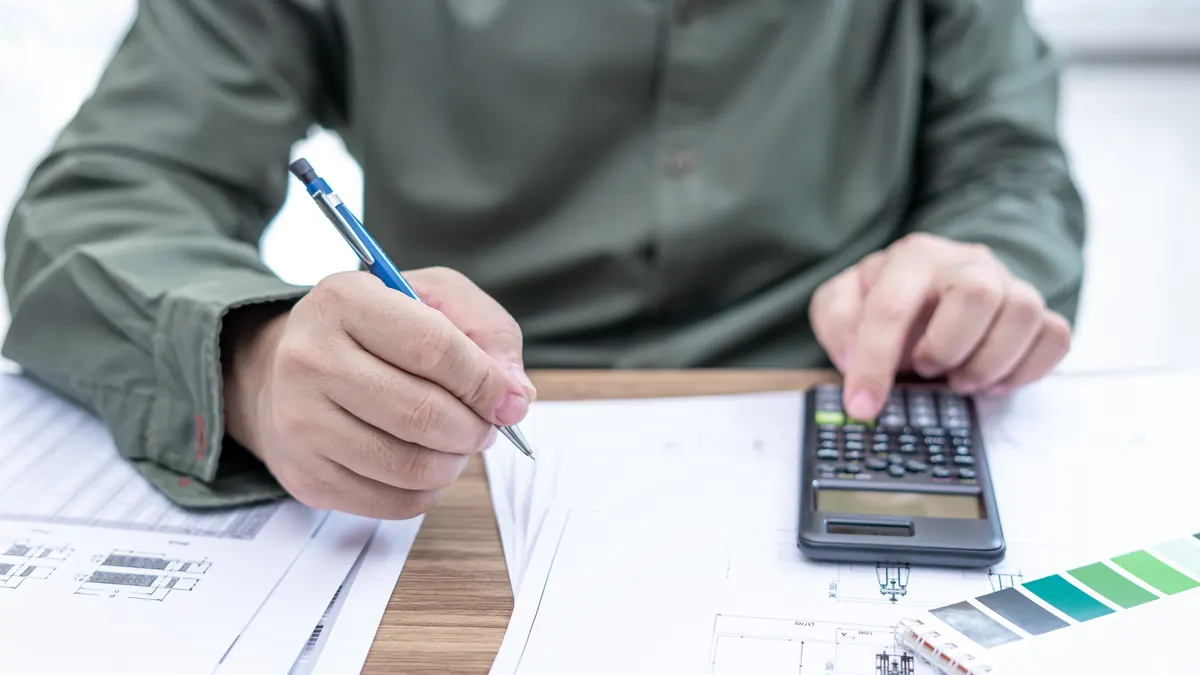 Hand with a pencil and calculator over drawings.
