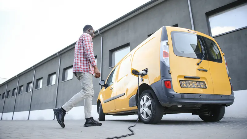 Electric van plugged in in front of an industrial building.